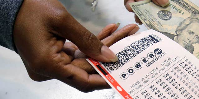 FILE - In this Jan. 13, 2016 file photo, a clerk hands over a Powerball ticket for cash at Tower City Lottery Stop in Cleveland.