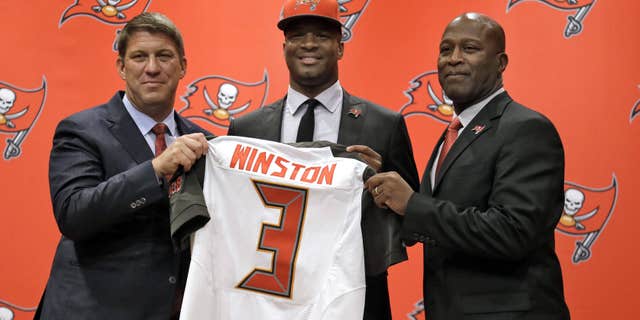 May 1, 2015: Tampa Bay Buccaneers first-round draft pick Jameis Winston, center, holds his jersey as he stands with general manager Jason Licht, left, and head coach Lovie Smith, right, during a news conference.