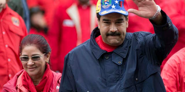 FILE - In this May 1, 2016 file photo, Venezuela's President Nicolas Maduro waves to supporters alongside first lady Cilia Flores during a labor day march in Caracas, Venezuela.