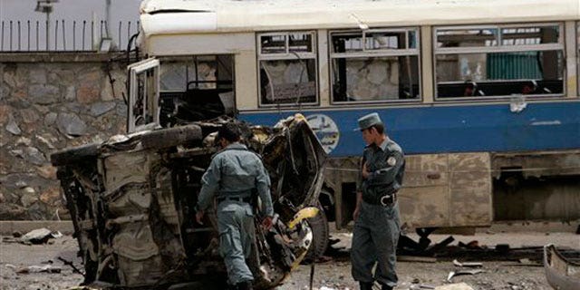 May 18: Afghan policemen look at the mangled remains of a vehicle after an attack in Kabul, Afghanistan.