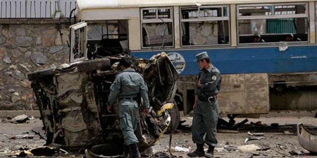 May 18: Afghan policemen look at the mangled remains of a vehicle after an attack in Kabul, Afghanistan.