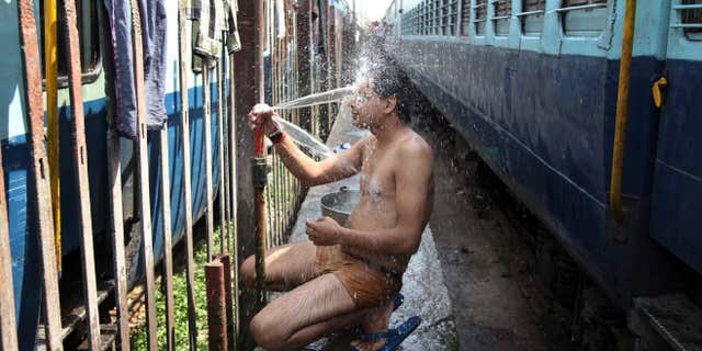 May 25, 2015: An Indian passenger takes a bath beside rail tracks on a hot summer day at a railway station in Jammu, India.