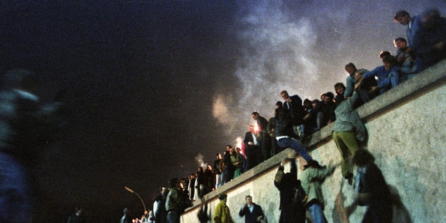 East German citizens climb the Berlin Wall at the Brandenburg Gate after the opening of the border was announced early Nov. 9, 1989.