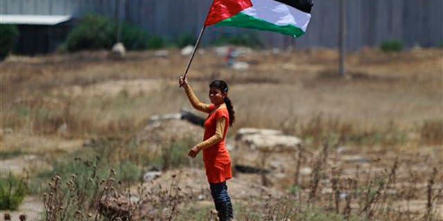 June 8: A Palestinian girl holding a national flag stands near the border line with Israel, background, during a weekly protest march against Israel, in Beit Hanoun, northern Gaza Strip.
