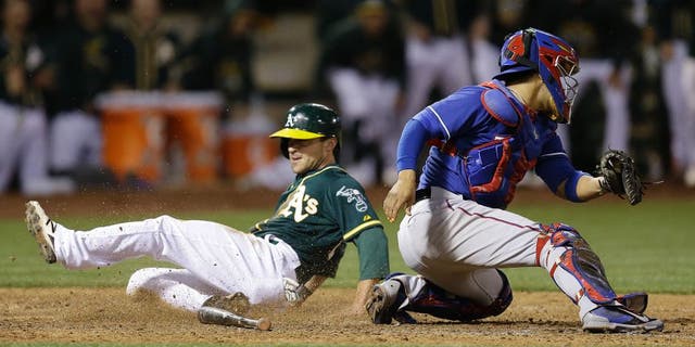 Oakland Athletics' Sam Fuld, left, slides to score behind Texas Rangers catcher Robinson Chirinos in the ninth inning of a baseball game Wednesday, June 10, 2015, in Oakland, Calif. The A's scored the winning run on the play, on a single by Josh Reddick. (AP Photo/Ben Margot)