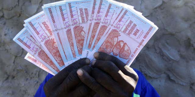 June 12, 2015: A man holds a handful of 5 Billion Zimbabwean dollar notes, in Harare.