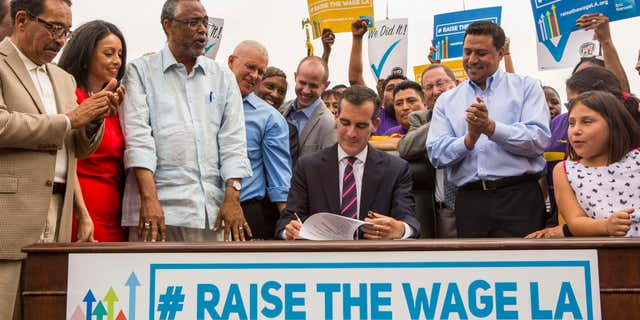 June 13, 2015: Los Angeles Mayor Eric Garcetti, center, joins members of the City Council and community leaders as he signs into law an ordinance that will gradually raise the minimum wage to $15 an hour by 2020, in at Martin Luther King Jr. Park in Los Angeles.