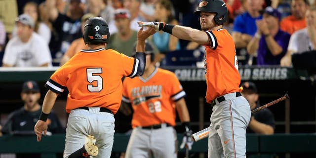Oklahoma State's Donnie Walton, left, is congratulated by Conor Costello after scoring on a single by Garrett Benge during the fourth inning of an NCAA College World Series baseball game against Arizona, Monday, June 20, 2016, in Omaha, Neb. (AP Photo/Nati Harnik)
