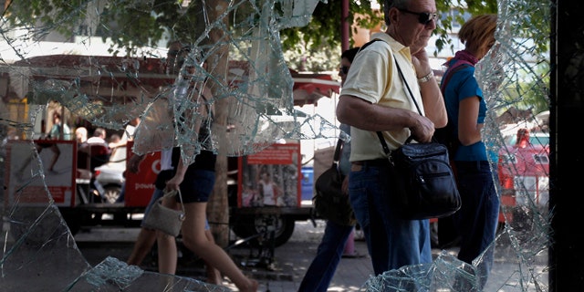 June 30: Athenians walk by a broken window of a building in central Athens.