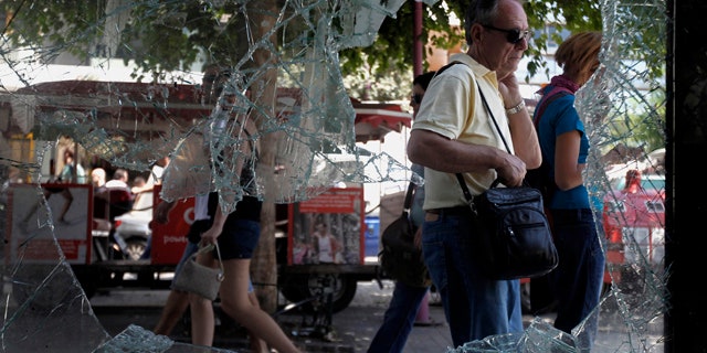 June 30: Athenians walk by a broken window of a building in central Athens.