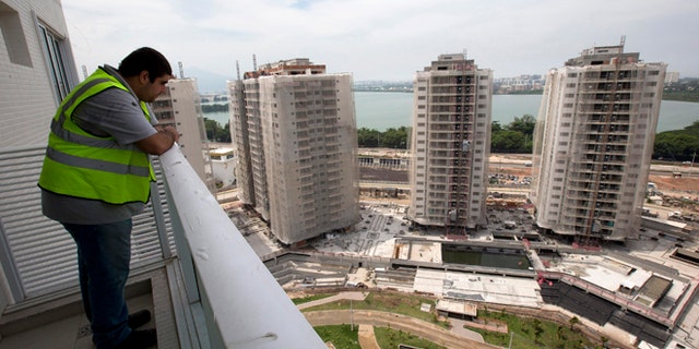 In this March 16, 2015 photo, a worker stands on the balcony of an apartment inside the Rio 2016 Olympic Games athletes village in Rio de Janeiro, Brazil. Christopher Gaffney, who spent 5 1/2 years in Rio researching the 2014 World Cup and Olympics, called the village "a transfer of wealth program from the public (treasury) to private construction firms." (AP Photo/Silvia Izquierdo)