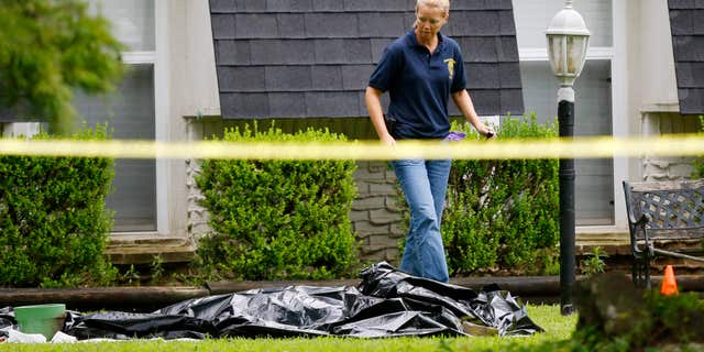 July 23, 2015: An investigator walks past a tarp covering a body in the front yard of a house in Broken Arrow, Okla.