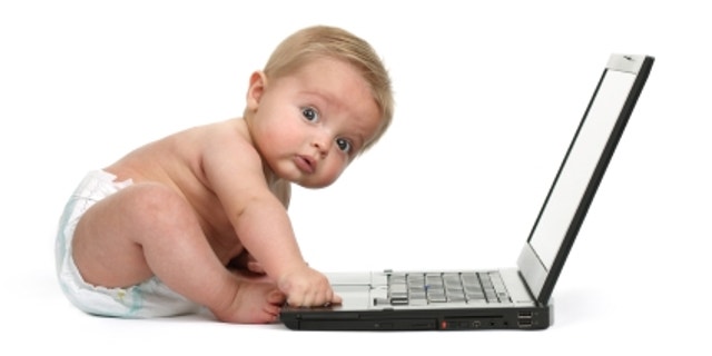 Surprised expression on a baby boys face whilst getting into mischief on a laptop computer