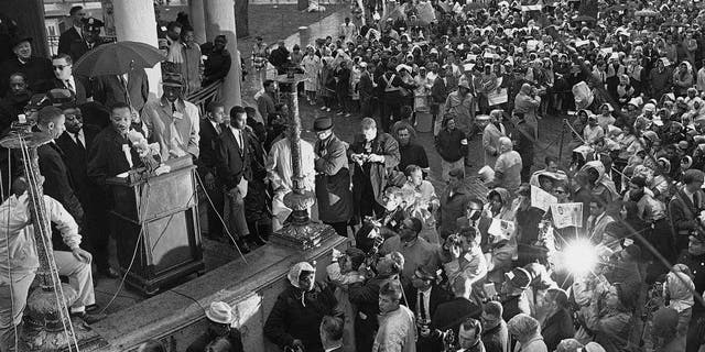 In this April 23, 1965 file photo, Dr. Martin Luther King Jr., under umbrella at left, addresses civil rights marchers on Boston Common after a march from the Roxbury section of the city to protest segregation in schools, unequal employment and housing concerns. Disparities between White and Black workers in lucrative fields in metro areas around the country still linger 50 years after King's death.
