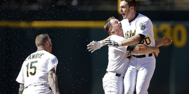Oakland Athletics' Stephen Vogt, center, lifts Mark Canha after Canha hit the game winning hit in the tenth inning of a baseball game against the Cleveland Indians, Sunday, Aug. 2, 2015, in Oakland, Calif. At left is A's Brett Lawrie (15). The A's won, 2-1.