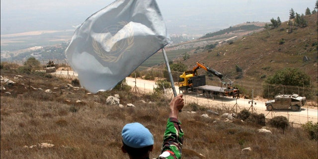 Aug. 3: A UNIFIL peacekeeper waves a U.N. flag as Israeli troops patrol the border in the southern border village of Adaisseh, Lebanon.