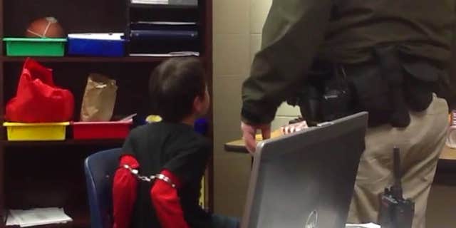Aug. 4, 2015: In this image made from video taken in August 2014, and provided by the American Civil Liberties Union, an 8-year-old boy struggles and cries out as he sits in a chair with handcuffs around his biceps and his arms locked behind him while a school resource officer stands nearby, at an elementary school in Covington, Ky.