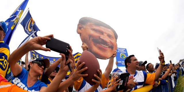 Fans watch the St. Louis Rams and the Dallas Cowboys participate in a joint NFL football training camp as one holds up a picture of Rans owner Stan Kroenke, Monday, Aug. 17, 2015, in Oxnard, Calif. (AP Photo/Mark J. Terrill)