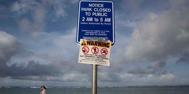 Aug. 25, 2015: Tourists walks near a warning sign posted on Waikiki Beach in Honolulu.