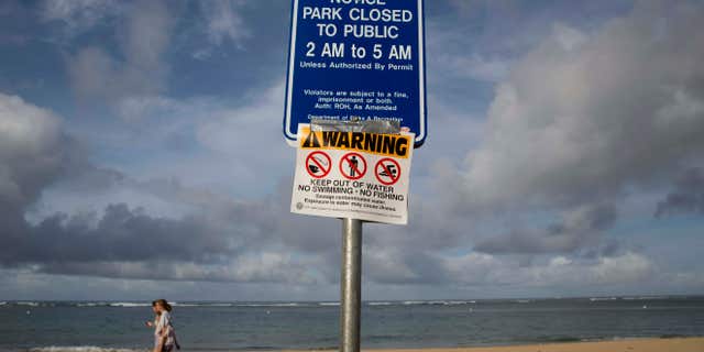 Aug. 25, 2015: Tourists walks near a warning sign posted on Waikiki Beach in Honolulu.
