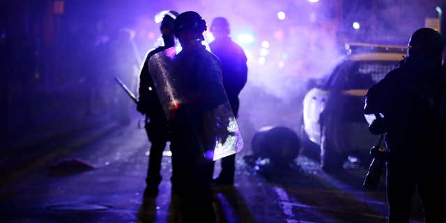 Nov. 25, 2014: Police officers watch protesters as smoke fills the streets in Ferguson, Mo. after a grand jury's decision in the fatal shooting of Michael Brown.