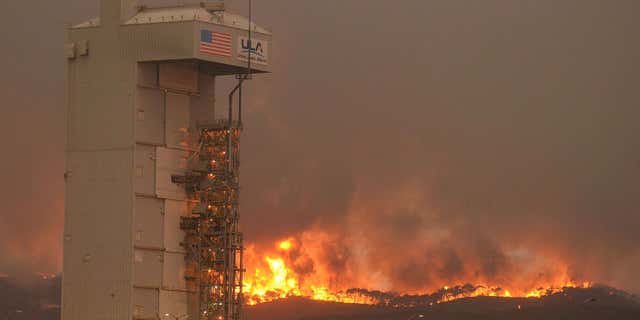 In this Monday, Sept. 19, 2016 photo provided by the Santa Barbara County Fire Department, a fire burns several miles behind Space Launch Complex-3, housing the Atlas V rocket & WorldView 4 satellite, at Vandenberg Air Force Base, Calif.