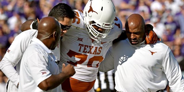 MANHATTAN, KS - OCTOBER 25: Head coach Charlie Strong (R) of the Texas Longhorns helps trainers take offensive guard Kent Perkins #76 against the Kansas State Wildcats during the first half on October 25, 2014 at Bill Snyder Family Stadium in Manhattan, Kansas. (Photo by Peter G. Aiken/Getty Images)