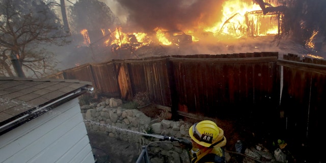 A Los Angeles County firefighter puts water on a burning roof during a wildfire in the Lake View Terrace area of Los Angeles, Tuesday.