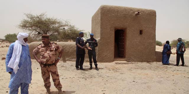 FILE - In this file photo taken Saturday, July 18, 2015, people attending a ceremony stand near a mausoleum, right, that was restored in Timbuktu, Mali after the 14 mausoleums in Mali’s northern historic city that had been destroyed by Islamic extremists in 2012 have been restored. An alleged Islamic extremist charged with involvement in the destruction of religious buildings has been arrested and was sent to the International Criminal Court early Saturday, Sept. 26, 2015 to face justice. (AP Photo/Baba Ahmed, File)