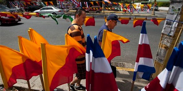 CORRECTS NAME TO LUIS GUILLERMO SOLIS - Men walk next to Costa Rican flags and political party flags, in San Jose, Costa Rica, Saturday, April 5, 2014. Costa Rica will vote on the Sundays runoff presidential election between Luis Guillermo Solis, presidential candidate of Citizen's Action Party and ruling party candidate Johnny Araya. (AP Photo/Moises Castillo)