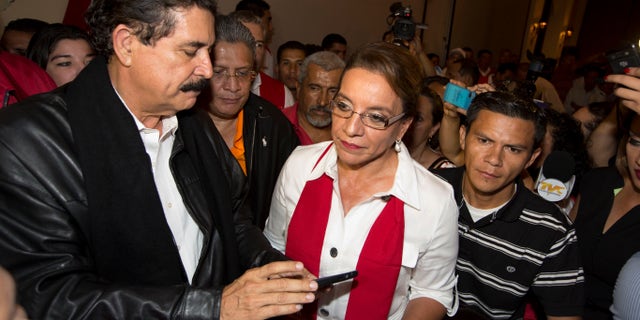 Free Party presidential candidate Xiomara Castro, center, and her husband, ousted President Manuel Zelaya, left, check information on his cell phone before the announcement of official election results in Tegucigalpa, Honduras, Sunday, Nov. 24, 2013. Hondurans cast ballots for a new president Sunday in a country reeling from violence, poverty and the legacy of a 2009 coup that ousted Zelaya. (AP Photo/Moises Castillo)