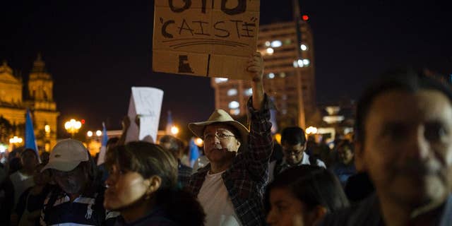 A protester holds a sign that reads in Spanish "Otto, you're down," referring to President Otto Perez Molina, after the arrest of his former Vice President Roxana Baldetti, who was arrested in connection with a corruption scandal, in the Central Park of Guatemala City, Friday, Aug. 21, 2015. Baldetti was detained Friday in connection with a customs corruption scandal that led to her resignation, and prosecutors announced they are also seeking to investigate the president in the matter. (AP Photo/Luis Soto)