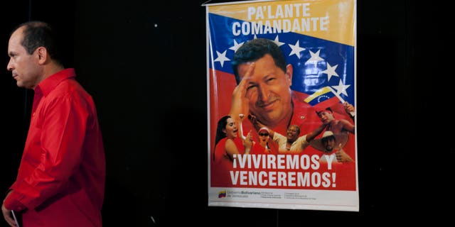 A poster of Venezuela's President Hugo Chavez that reads "Move forward commander, we will live and overcome" hangs as Venezuela's ambassador to Cuba Edgardo Antonio Ramirez stands by after a press conference by Cuban artists and intellectuals to show support for Chavez in Havana, Cuba, Monday, Jan. 7, 2013. Chavez hasn't spoken or appeared publicly since his Dec. 11 operation in Cuba, his fourth surgery for an undisclosed type of pelvic cancer. Speculation about the leader's condition has grown since the operation. (AP Photo/Ramon Espinosa)