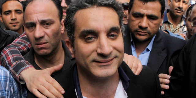 FILE - In this Sunday, March 31, 2013 file photo, a bodyguard secures popular Egyptian television satirist Bassem Youssef, who has come to be known as Egypt's Jon Stewart, as he enters Egypt's state prosecutors office to face accusations of insulting Islam and the country's Islamist leader in Cairo, Egypt. Youssef's show is scheduled to air Friday night, April 5, 2013, for the first time since he appeared in court last Sunday.(AP Photo/Amr Nabil, File)