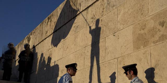 The shadow of a demonstrator waving a flag is cast on a wall as Greek police officers secure the Greek Parliament during a protest in central Athens, Wednesday, June 15, 2016. Several thousand anti-government protesters gathered in central Athens Wednesday to demand the resignation Prime Minister Alexis Tsipras, accusing his government of breaking promises to end austerity and sinking the country deeper into financial distress.(AP Photo/Petros Giannakouris)