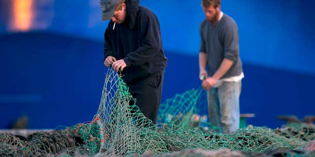 FILE - In this Nov. 15, 2013 file photo, fishermen Ed Stewart, left, and Tannis Goodsen mend groundfishing nets on Merrill Wharf in Portland, Maine.