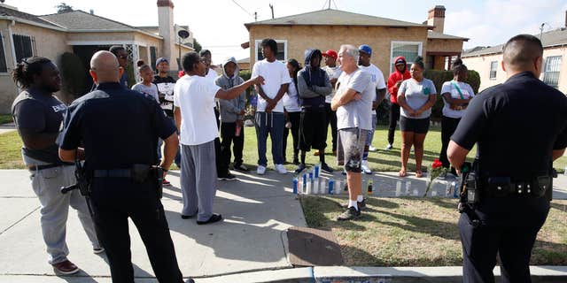 Oct. 2, 2016: Los Angeles Police officers speak to neighbors and members of the community gathered around a makeshift memorial outside a residence.