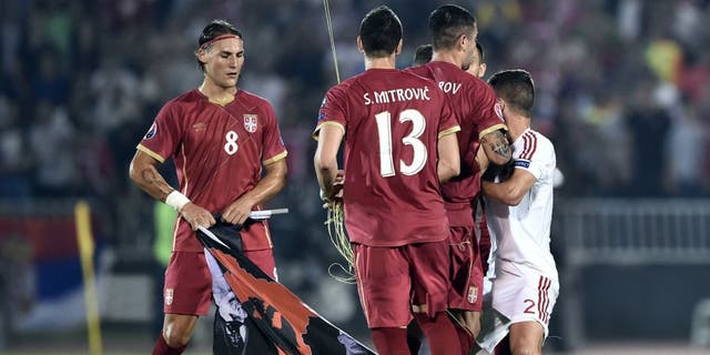 Serbia's midfielder Nemanja Gudelj (L) holds a flag with Albanian national symbols pulled down by Serbia's defender Stefan Mitrovic (C) from a remotely operated drone flown over the pitch during the EURO 2016 group I football match between Serbia and Albania in Belgrade on October 14, 2014. AFP PHOTO / ANDREJ ISAKOVIC (Photo credit should read ANDREJ ISAKOVIC/AFP/Getty Images)