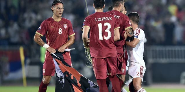 Serbia's midfielder Nemanja Gudelj (L) holds a flag with Albanian national symbols pulled down by Serbia's defender Stefan Mitrovic (C) from a remotely operated drone flown over the pitch during the EURO 2016 group I football match between Serbia and Albania in Belgrade on October 14, 2014. AFP PHOTO / ANDREJ ISAKOVIC (Photo credit should read ANDREJ ISAKOVIC/AFP/Getty Images)