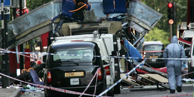 In this July 7, 2005 file photo, a forensic officer walks next to the wreckage of a double decker bus with its top blown off and damaged cars scattered on the road at Tavistock Square in central London.