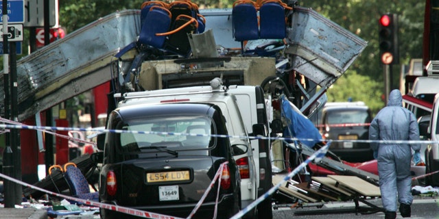 In this July 7, 2005 file photo, a forensic officer walks next to the wreckage of a double decker bus with its top blown off and damaged cars scattered on the road at Tavistock Square in central London.