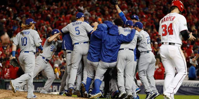 As Washington Nationals' Bryce Harper (34) walks from the field, the Los Angeles Dodgers celebrate a 4-3 win in Game 5 of a baseball National League Division Series, at Nationals Park early Friday, Oct. 14, 2016, in Washington.