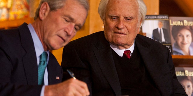 Former U.S. President George W. Bush, left, signs a copy of his book "Decision Points" for Billy Graham, right, at the Billy Graham Library in Charlotte, North Carolina, on Dec. 20, 2010.