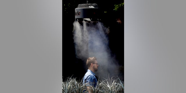 A man stands under a misting machine, Monday, June 19, 2017 in Tempe, Ariz. The forecast calls for a high of 118 on Monday and 120 on Tuesday in Phoenix. (AP Photo/Matt York)