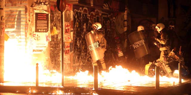 Nov. 15, 2016: Police officers walk past flames from a fire bomb thrown by demonstrators during a protest against the visit of US President Barack Obama in Athens.