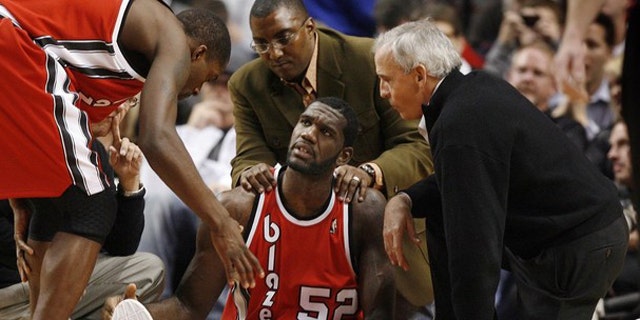 Portland Trail Blazers center Greg Oden (52) receives encouragement from teammate Martell Webster (L) as medical personel attend to his broken left leg during the first quarter of their NBA basketball game in Portland, Oregon on December 5, 2009.