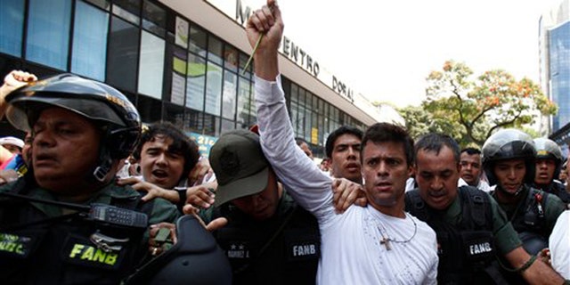 Opposition leader Leopoldo Lopez, dressed in white and holding up a flower stem, is taken into custody by Bolivarian National Guards, in Caracas, Venezuela, Tuesday, Feb 18, 2014. Lopez re-emerged from days of hiding to address an anti-government demonstration and then he turned himself in to authorities Tuesday. Speaking to some 5,000 supporters with a megaphone, Lopez said that he doesn't fear going to jail to defend his beliefs and constitutional right to peacefully protest against President Nicolas Maduro. (AP Photo/Alejandro Cegarra)