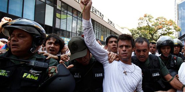 Opposition leader Leopoldo Lopez, dressed in white and holding up a flower stem, is taken into custody by Bolivarian National Guards, in Caracas, Venezuela, Tuesday, Feb 18, 2014. Lopez re-emerged from days of hiding to address an anti-government demonstration and then he turned himself in to authorities Tuesday. Speaking to some 5,000 supporters with a megaphone, Lopez said that he doesn't fear going to jail to defend his beliefs and constitutional right to peacefully protest against President Nicolas Maduro. (AP Photo/Alejandro Cegarra)