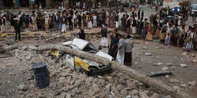 People stand near a vehicle destroyed following airstrikes by the Saudi-led coalition in Sanaa, Yemen, Tuesday, July 14, 2015. The coalition has been targeting the Iran-allied Houthis since March in a bid to stop their power grab across the country. Yemeni forces battling the Shiite rebels in the country's south said they took control on Tuesday of the airport in the strategic port city of Aden. (AP Photo/Hani Mohammed)