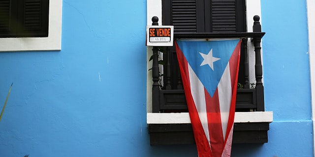 SAN JUAN, PUERTO RICO - JULY 01: A for sale sign is seen hanging from a balcony next to a Puerto Rican flag in Old San Juan as the island's residents deal with the government's $72 billion debt on July 1, 2015 in San Juan, Puerto Rico. Governor of Puerto Rico Alejandro GarcÃa Padilla said in a speech recently that the people of Puerto Rico will have to make sacrifices and share the responsibilities to help pull the island out of debt. (Photo by Joe Raedle/Getty Images)